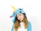 Pretty blonde girl with cozy blue unicorn costume is posing in the studio in front of white wall and is happy