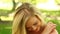 Pretty blonde relaxing in the park smiling at the camera while smelling a flower