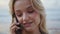 Pretty blonde talking mobile phone at ocean shore. Closeup beautiful woman face