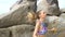 Pretty blonde woman exercising using jumping rope between the rocks near the sea during summer day