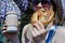 Pretty blonde woman holding cup of coffee and sweet pretzel in a