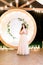 Pretty bride with rustic wedding wreath on head stands on the background of arch and decorations. Outdoor wedding