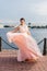 Pretty brunette caucasian model waving hem of pastel pink beaded dress on quay