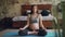 Pretty brunette expectant mother is relaxing in lotus position on mat on floor practising hatha yoga with hands on her