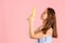 A pretty brunette holds a banana like a gun on a pink background. Copy space