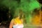 Pretty brunette woman with short hair posing with exploding green and orange Holi paint