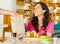 Pretty brunette woman wearing pink shirt sitting by table inside bakery, receiving brown paper bag from waiter and