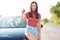 Pretty brunette young European woman shows car key, rejoices new purchase, poses near new automobile, dressed in casual t shirt