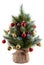 Pretty bushy Christmas pine tree in a pot wrapped in cloth. Decorated with bright colorful balls, cones, and red berries. Tips of