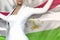 Pretty business woman holds Tajikistan flag in hands behind her back on the office building background - flag concept 3d