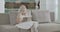 Pretty Caucasian girl in elegant white dress sitting on coach and reading as Santa Claus walking at the background. Cute