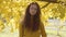 Pretty caucasian girl with long curly hair standing on the background of yellow leaves. Redhead child in mustard sweater