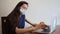 Pretty Caucasian woman with brown hair works remote on laptop at home. Cute girl in medical face mask in office clothes typing