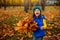 Pretty child baby girl with collected autumnal maple leaves bouquet cutely smiles and laughs standing among golden fallen leaves