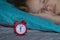 Pretty child girl sleeping on the background of a red alarm clock that will wake her up in the morning.