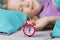 Pretty child girl sleeping on the background of a red alarm clock that will wake her up in the morning.