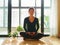 Pretty Chinese young woman meditating at home, sitting on floor with furry cushion in sun light, exercise, Lotus pose, prayer