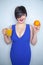 Pretty chubby brunette with an orange fruit in her hand and with glass cup with healthy juice standing in blue dress on white back