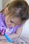 Pretty concentrated little girl in pale purple shirt drawing in book