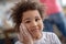 Pretty curly-haired kid touching her cheek with hand stained with flour and looking happy