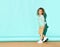 Pretty curly little girl standing near the wall with hands in pockets and calm serious face. Full length portrait