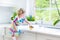 Pretty curly toddler girl in colorful dress washing dishes