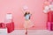 Pretty excited amazing little girl with long brunette hair jumping with balloon suround colorful giftboxes on pink