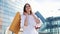 Pretty fashion model in white dress poses with shopping bags before a modern glass building