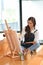 Pretty female hipster artist sitting on floor, painting on canvas