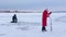 Pretty fisherwoman in red warm jacket and felt boots makes hole for ice fishing with help ice drill on frozen river