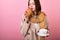 A pretty Frenchwoman of a beautiful woman who eats a croissant and drinks tea or coffee on a pink background