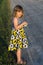 Pretty frowning little girl in summer dress standing next to a dirt road