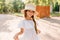 Pretty girl in big straw hat playing with her white dress while posing in park with wooden fence on background. Portrait