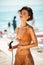 Pretty girl in bikini using hose pipe on beach. Portrait of lady in beige swimsuit rinsing beach sand off her body on