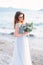 Pretty girl in blue wedding dress holding the bouquet of flowers at the beach of Garda Lake