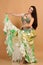 A pretty girl brunette who dances go-go and belly dance, stretching posing in studio in green arabian dress on a beige background