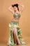 A pretty girl brunette who dances go-go and belly dance, stretching posing in studio in green arabian dress on a beige background