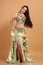 A pretty girl brunette who dances go-go and belly dance, stretching posing in studio in green arabian dress on a beige background