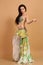 A pretty girl brunette who dances go-go and belly dance, stretching posing in studio in green arabian dress on a beige background