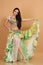 A pretty girl brunette who dances go-go and belly dance, stretching posing in studio in green arabian dress on a beige background