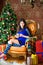 Pretty girl with a cup of coffee sits in a chair near the festive Christmas tree