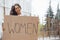 Pretty girl with curly hair stands with handmade feminist poster in hands