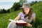 Pretty Girl With Daisy Flower In Her Mouth Enjoying Reading Interesting Book In The Grass