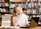 Pretty girl in library typing on laptop and talking on the phone