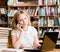 Pretty girl in library typing on laptop and talking on the phone