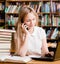 Pretty girl in library typing on laptop and talking on the phone