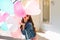 Pretty girl with long curly hair in sunglasses hides behind a bunch of balloons and sends an air kiss. Portrait of