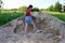 pretty girl in red T-shirt and denim shorts is digging the sand with big shovel. Landscape works,