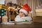 Pretty girl in Santa hat writing letter and joyfully lying at table near the pile of presents