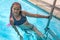 Pretty girl swimmer with pink dreadlocks hairstyle standing near ladder in swimming pool